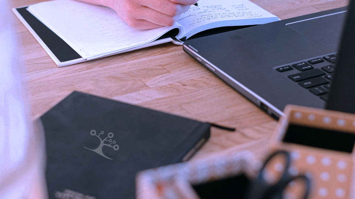 A photo of a notebook, laptop, and book on a table top.