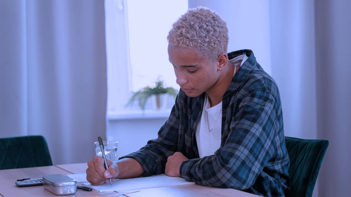 A high school student sitting at a desk writing on a paper.