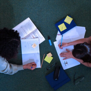 An overhead shot of two girls laying on the floor doing homework.