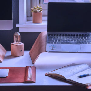 A desk with lapton on a stand and a open notebook and other desk items.