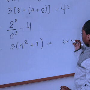 A boy writing math problems on a whiteboard with a marker.