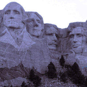 Mount Rushmore National Memorial featuring the carved faces of four U.S. presidents on a granite cliff, with trees at the base under a partly cloudy sky.
