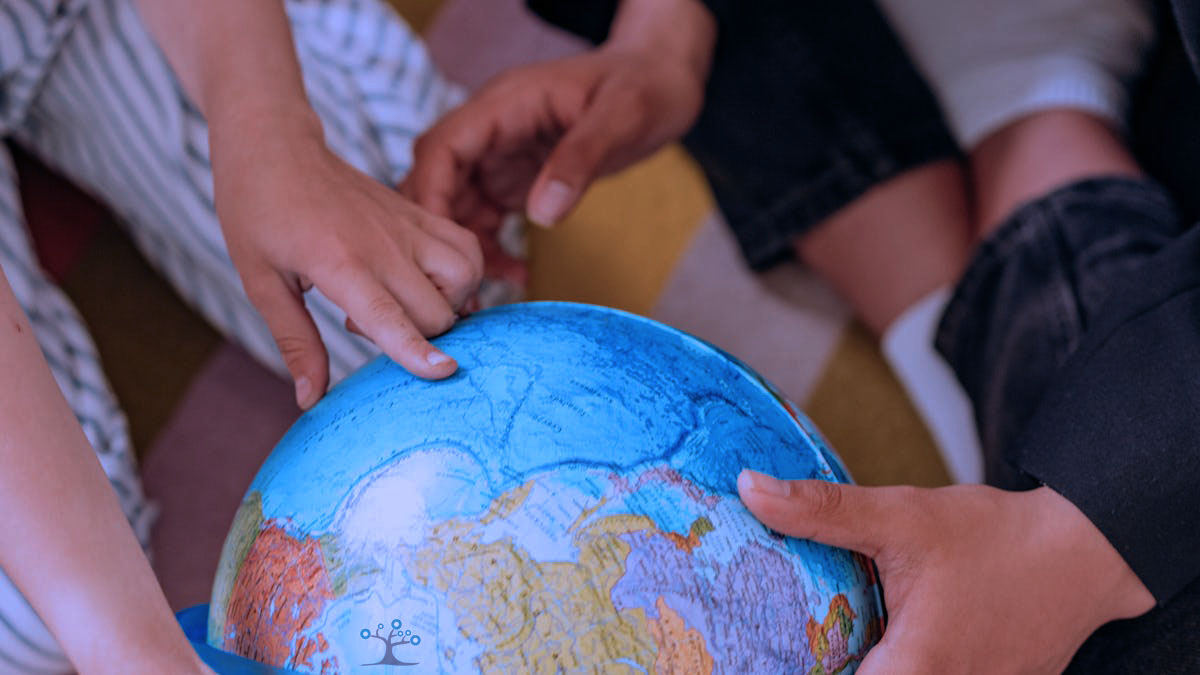 Small hands on a globe pointing to a spot in the ocean.