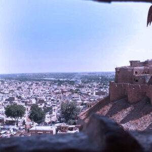 View of a cityscape with many low-rise buildings, seen through a stone window or opening in an old fort or wall. The structure has brown stone walls, and the landscape stretches into the distance under a clear sky.