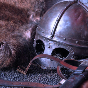 A metal helmet and sword on top of chains and next to a hide.