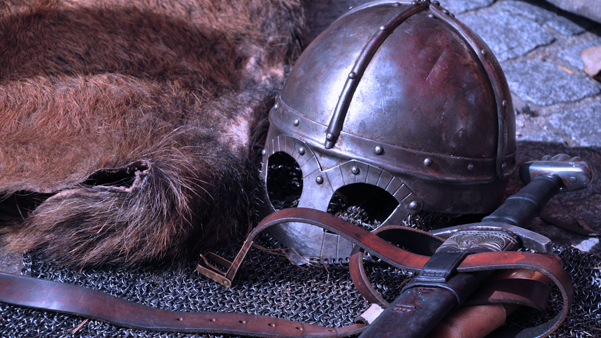 A metal helmet and sword on top of chains and next to a hide.