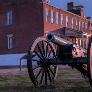 A large canon sitting in a field in front of an old red building.