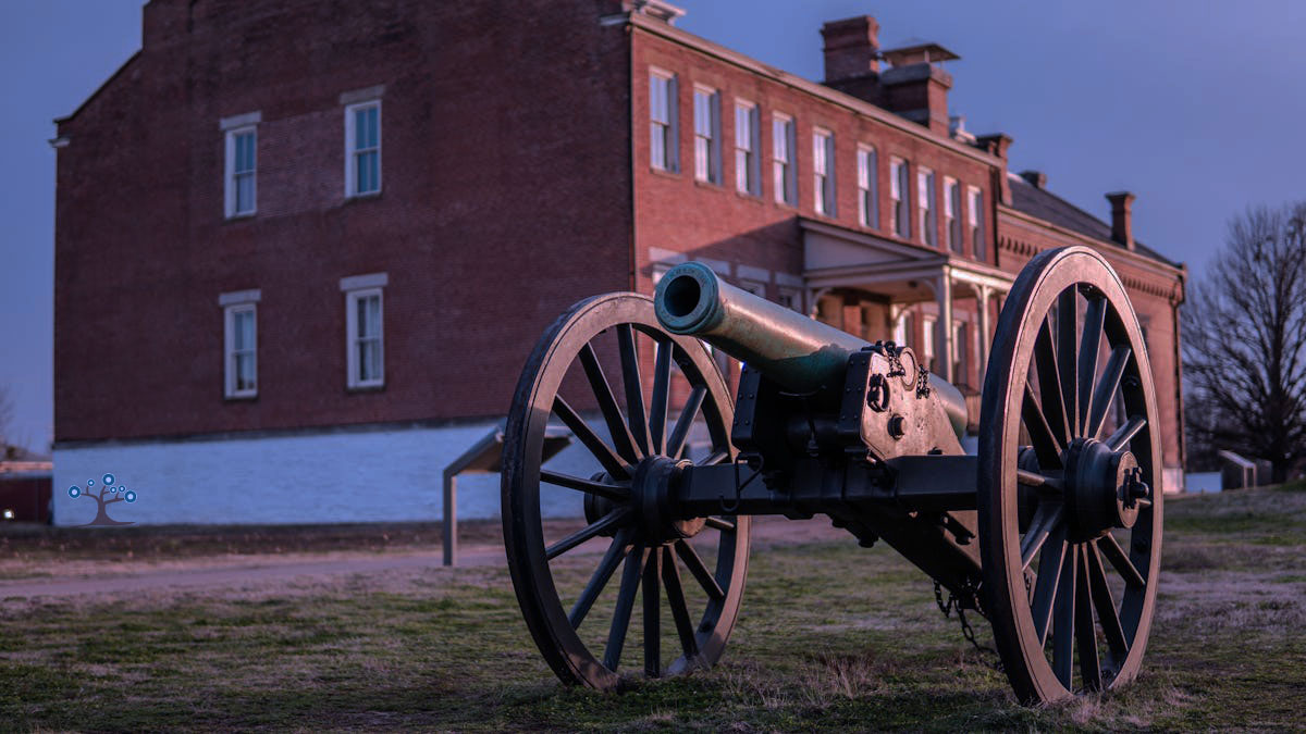 A large canon sitting in a field in front of an old red building.
