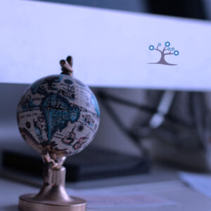 A minature globe sitting on a desk in front of monitor.