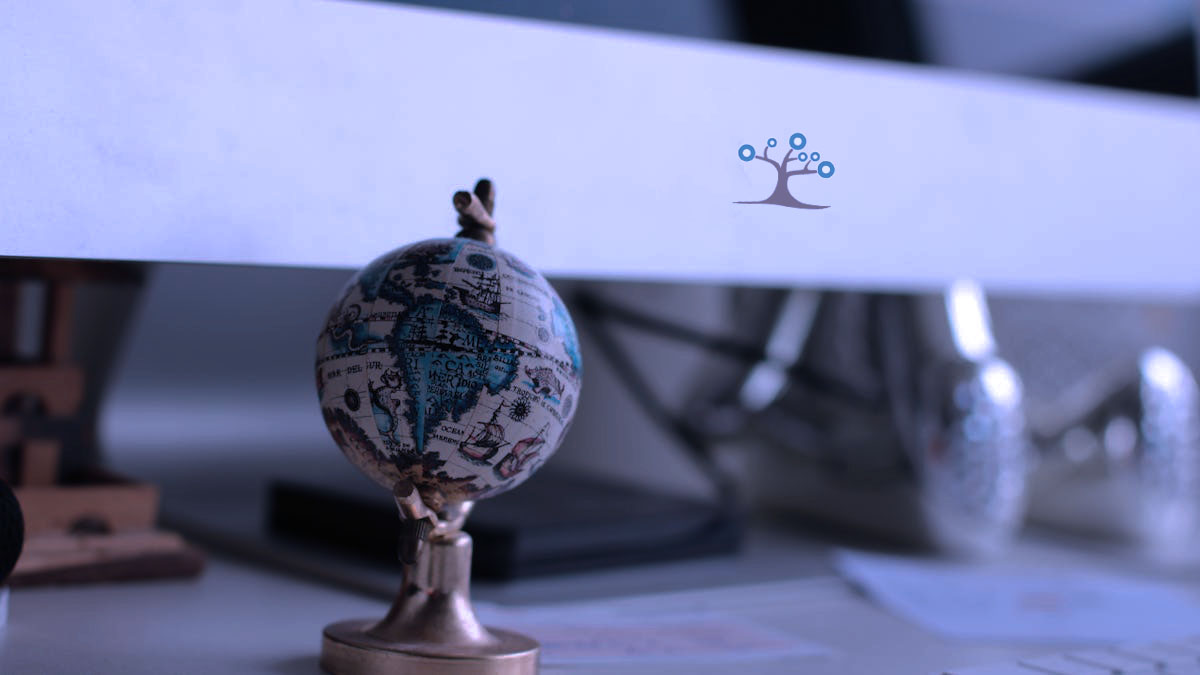 A minature globe sitting on a desk in front of monitor.