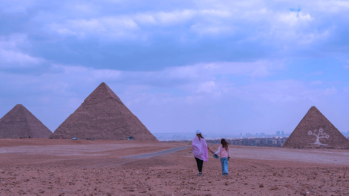 a mother and daughter walking in the desert towards the Pyramids of Giza.